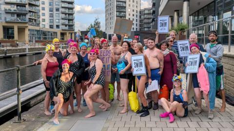 A group of people in swimming costumes pose for a photo. Some of them are holding banners which read 'Right to Swim'.