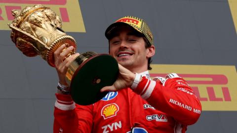 Ferrari's Charles Leclerc smiles while holding the British Grand Prix winner's trophy