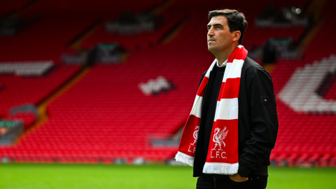 Andoni Iraola stands in the Liverpool FC stadium wearing a team scarf