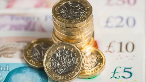 A generic image of British pound coins on top of cash notes.
