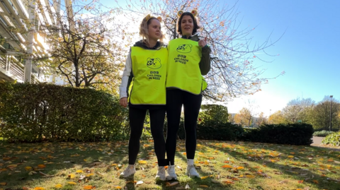 Katie Tyler and Sophie Drew, who are tied together and wearing high visibility vests and Pudsey ears.