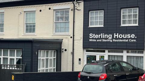 The outside of Sterling House on Thorpe Road in Norwich, a specialist dementia care home. The building has a white painted brick exterior and a sign with white writing says, Sterling House. White and Sterling Residential Care.