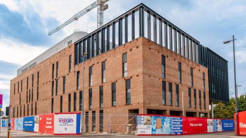 The three-storey eye hospital. It is a red-brick building with several windows on each floor. The area around the base of the hospital is fenced off.