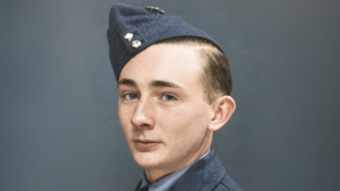 A man in a blue military side cap and blue uniform jacket, with a shirt and tie underneath. He is looking to the camera