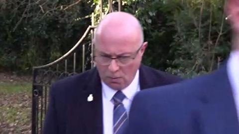 PC Mark Roberts leaving Durham Crown Court. He is wearing a dark suit and a blue striped tie. He is bald, is wearing glasses and looking down.