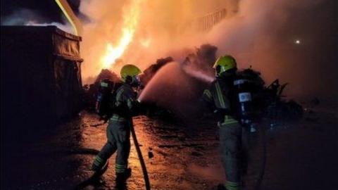 Two firefighters with water blasting from their hoses at a mound with flames and smoke