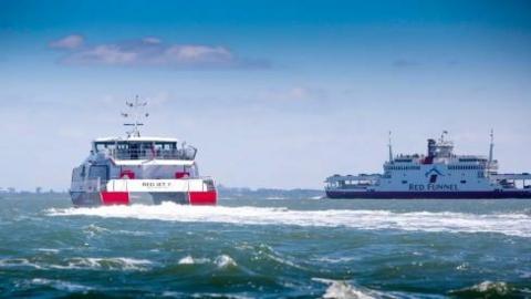 Two red funnel ferries on the water. The sky above is blue and the water is choppy.