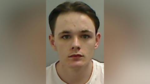 Mugshot of Finn-Gibbs. He is clean shaven with a spotty face and brown hair swept back.