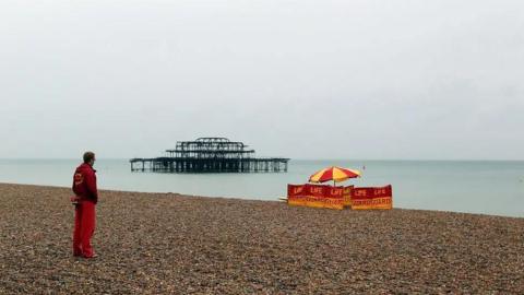 A lifeguard looks out to sea, with a station closer to the sea.