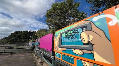The empty top story of the Cathedral and Quay car parkon the left and graffiti in the foreground on the right showing hands holding a mobile phone with an orange border.