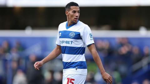 Isaac Hayden walking on the pitch during a match for QPR. He is wearing QPR's blue and white striped kit