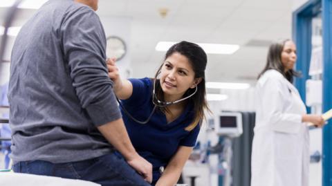 A hospital worker places a stethoscope on a patient's chest. 