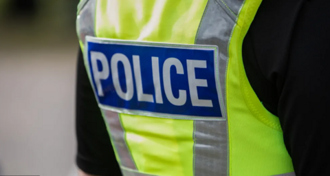 The back of a police officer who is wearing a fluorescent police vest.