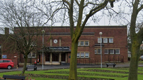 A large building has a sign on the front saying 'Thornton Little Theatre'.