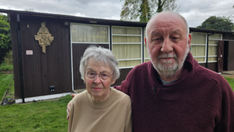 A woman with short grey hair and a bald man with greying beard stood outside a church