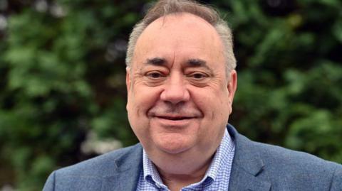 Alex Salmond wearing a blue checked suit jacket and a white checked shirt with the collar open