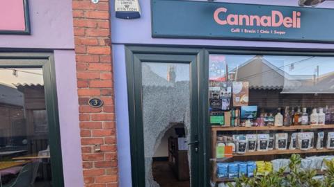 Llun o ffenestr flaen caffi wedi'i chwalu a gwydr ar y llawr.