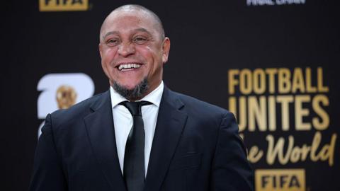 Roberto Carlos smiles for a photo while wearing a suit at the Fifa World Cup draw