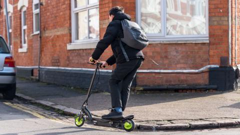 A boy riding an e-scooter on a residential street in the united Kingdom
