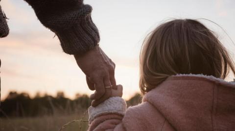 A young girl holding an adult's hand, looking over a field