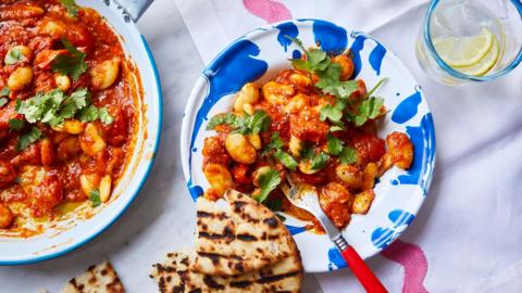 A pan and a plate containing butter beans cooked in a curried tomato sauce with fresh coriander on top and toasted naan alongside