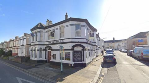 A white building with black horizontal stripes painted across it. The Grenville is painted in black lettering. The building is two storeys.