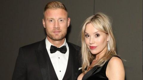 Freddie Flintoff, who has short light brown hair swept back and a light beard, is standing next to his wife Rachael. He is wearing a black tuxedo with a white shirt while she is wearing a dark dress. Rachael has light blonde hair and is smiling. 