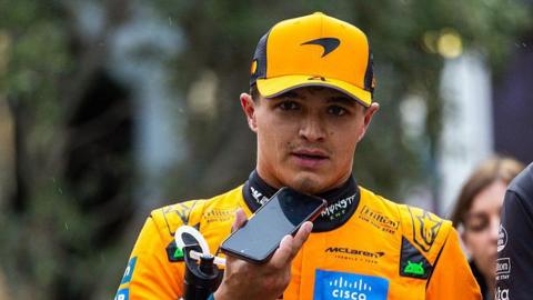 Lando Norris walking in his McLaren suit after qualifying in Baku and talking into a mobile phone