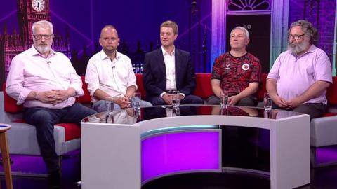 Bury North and Bury South candidates Jeff Armstrong (Reform), James Daly (Conservative), James Frith (Labour), Andrew Page (Liberal Democrats) and Owain Sutton (Green) sit on a sofa in front of an image of 10 Downing Street and the Palace of Westminster and behind a mirrored table with glasses of water on it