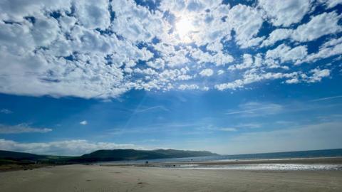 Speckled cloud and blue sky over the coast with headland sand and sea beneath - the tide is out 