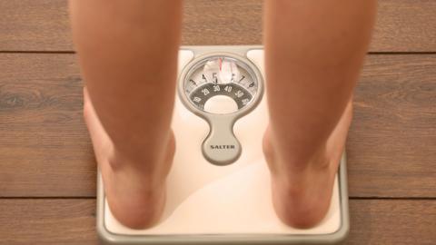 An image of someone using a set of weighing scales. Only part of their legs and feet are visible.