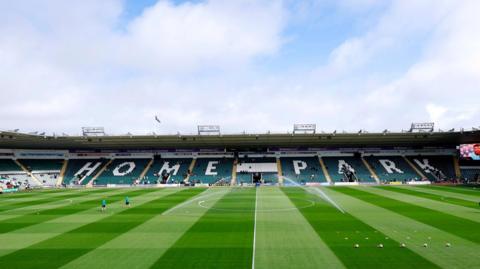 A general view of Home Park. There is a green pitch with people on it and in the background, in the stands is the words 'HOME PARK'