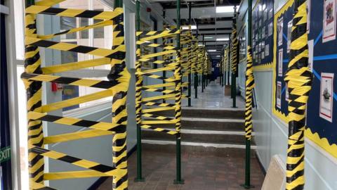 Support poles wrapped in hazard tape holding up the ceiling in the school corridoor