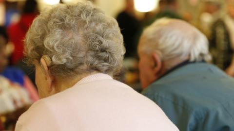 Two elderly people sitting next to each other , seen from the back.