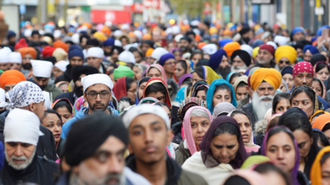 Lots of people wearing a variety of head scarfs and head dresses, walking along a street 