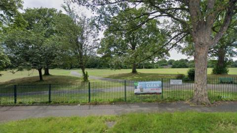 Firth Park in Sheffield, showing the gate and pathway and several large trees 