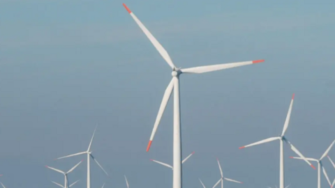 Offshore wind farm. there are about eight white wind turbines with orange on the tips. The background a blue sky.