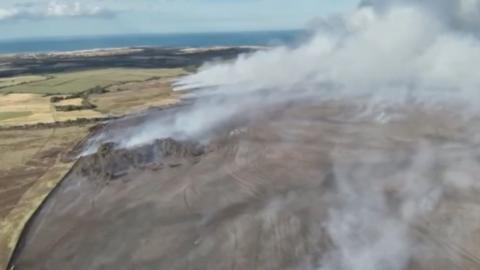 Smoke rises from a moorland, aerial shot