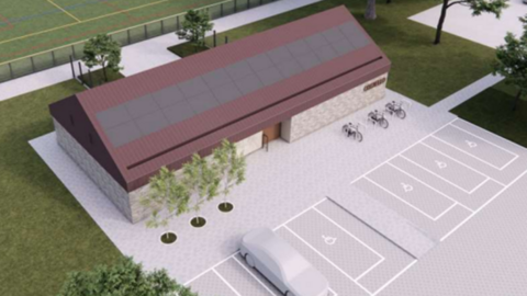 A computer-generated artist's impression of a modern, single-story building with solar panels on its sloped roof and stone brick walls. It is surrounded by a paved area with trees, bike racks and a small car park that includes disabled spaces. One space is occupied by a white cartoon car. Nearby, there is a grassy area and a fenced sports field.