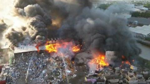 A fire at what looks like a scrapyard - with piles of burning rubbish and several buildings ablaze.