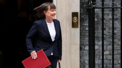 Llun o'r ysgrifennydd Jo Stevens yn cerdded allan yn gafael ar ffeil goch. 