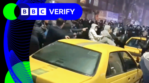 Protesters and security forces gather in the street around yellow cars in Iran's Urmia