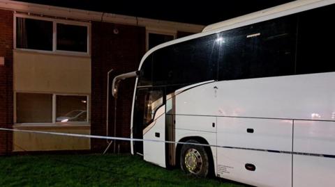 A white coach on a patch of grass right up against a two-storey building