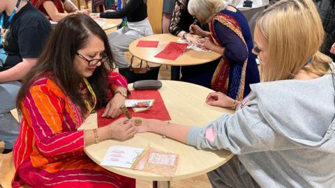 A woman drawing a henna tattoo on a college pupil