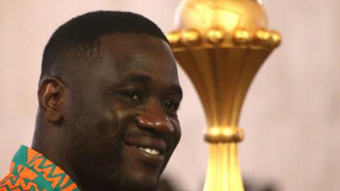 Emerse Fae smiles with the Africa Cup of Nations trophy in the background