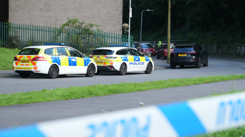 The police cordon and cars parked on Cwm Road