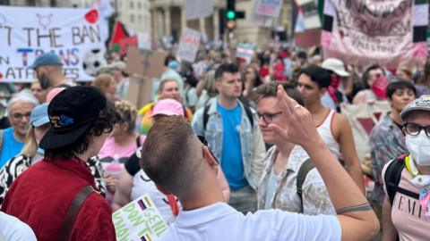 Lots of different people taking part in London Trans+ Pride. Some banners can be seen in the background
