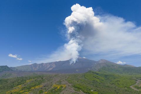 Mount Etna erupts in front of a green landscape in Italy