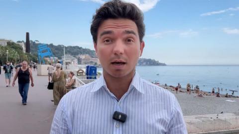 Man in a striped shirt with a beach behind him