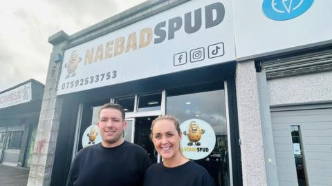 David Groves and Angela McCall, smiling at camera, outside the NaeBadSpud shop.